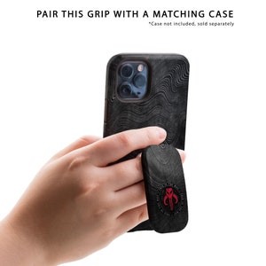 May include: A black phone case with a wood grain pattern and a black phone grip with a red Mandalorian symbol. The text "This is the way" is printed around the symbol.