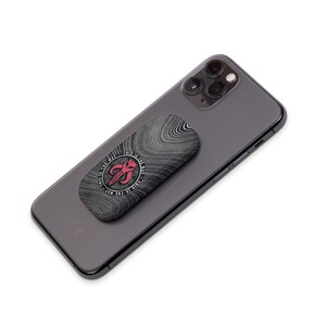 May include: A black and white phone grip with a red Mandalorian symbol and the text "This is the way" in a circle around the symbol. The grip is attached to a black smartphone.