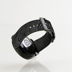 May include: Black smartwatch with a black patterned band. The watch face is visible and has a white circle in the center.