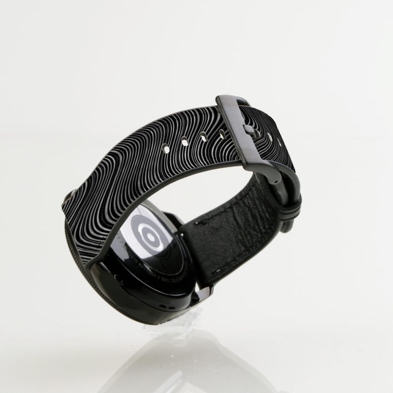 May include: Black smartwatch with a black patterned band. The watch face is visible and has a white circle in the center.