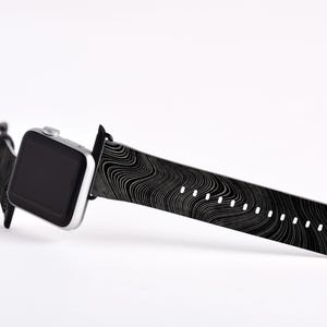 May include: A black and white patterned Apple Watch band with a silver Apple Watch.