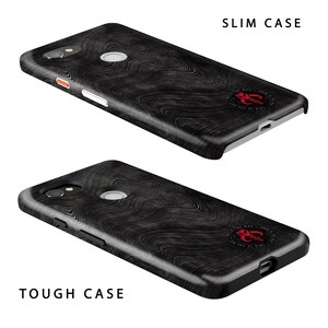 May include: Two phone cases with a black and white wood grain design. The top case is labelled "SLIM CASE" and the bottom case is labelled "TOUGH CASE". Both cases feature a red and white logo with the text "This is the way" and a symbol.