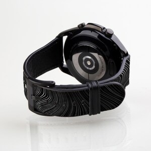 May include: Black smartwatch with a black leather band featuring a wavy pattern. The watch face is black with a silver ring around the edge. The watch is on a white background.