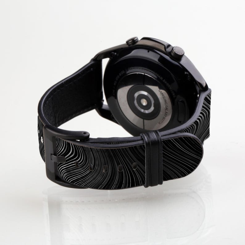 May include: Black smartwatch with a black leather band featuring a wavy pattern. The watch face is black with a silver ring around the edge. The watch is on a white background.