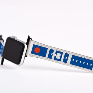 May include: A white Apple Watch band with a blue and red design. The band features a red circle on a blue background, followed by a pattern of blue squares and rectangles.