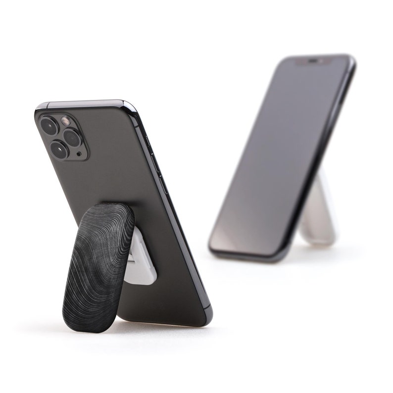 May include: Two black smartphones with a textured black phone stand. The stand is attached to the back of the phone and allows the phone to stand upright.