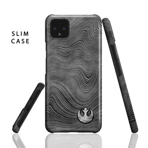 Puede incluir: Una funda de tel&eacute;fono negra con un s&iacute;mbolo blanco de la Alianza Rebelde y un patr&oacute;n ondulado de madera. La funda est&aacute; dise&ntilde;ada para un tel&eacute;fono Google Pixel y dice "SLIM CASE" en la esquina superior izquierda.