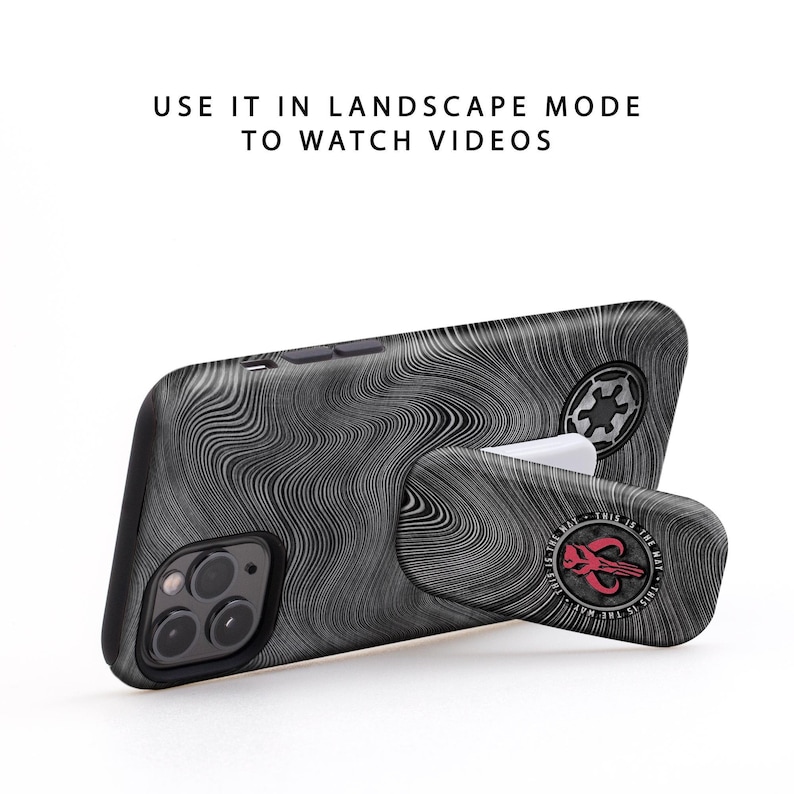 May include: A black phone case with a swirling pattern and a pop-out stand. The stand has a red Mandalorian symbol with the text "This is the way" around it.