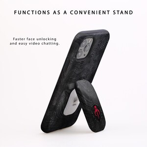 May include: A black phone case with a wood grain pattern and a kickstand. The kickstand is in the up position, allowing the phone to stand upright. The case has a red and white logo on the back.