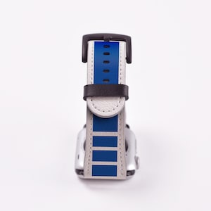 May include: A white and blue Apple Watch band with a black buckle. The band has a blue stripe pattern.