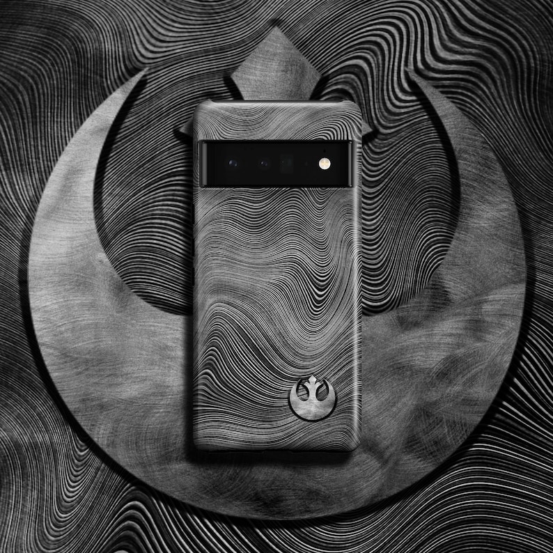 Puede incluir: Una funda de tel&eacute;fono negra con un s&iacute;mbolo de la Alianza Rebelde y un dise&ntilde;o ondulado texturizado. La funda est&aacute; delante de un fondo plateado con un patr&oacute;n ondulado.