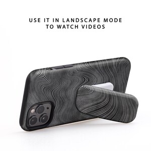 Puede incluir: Funda de tel&eacute;fono negra con un patr&oacute;n de remolino blanco y un soporte integrado. "USE IT IN LANDSCAPE MODE TO WATCH VIDEOS" est&aacute; escrito en blanco sobre un fondo blanco.