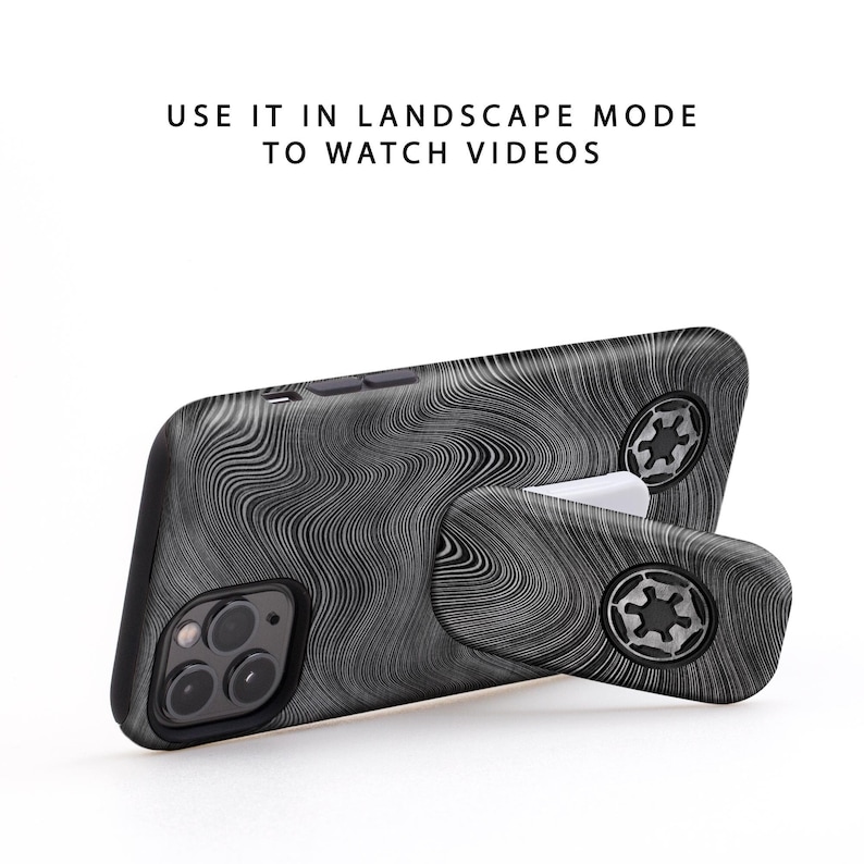 May include: A black and gray phone case with a swirling pattern, propped up by a white stand. The case has a camera and buttons visible. The text on the image reads: "USE IT IN LANDSCAPE MODE TO WATCH VIDEOS."