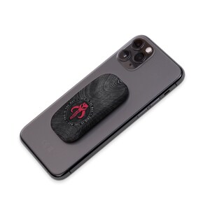 May include: A black phone case with a wood grain pattern and a red Mandalorian symbol. The text "This is the way" is written around the symbol. The case is attached to a black smartphone.