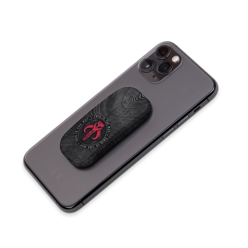 May include: A black phone case with a wood grain pattern and a red Mandalorian symbol. The text "This is the way" is written around the symbol. The case is attached to a black smartphone.