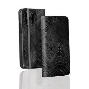 Może przedstawiać: Czarne etui na telefon z falistym, abstrakcyjnym wzorem. Etui ma klapkę, kt&oacute;ra składa się na ekran telefonu i pasek do zamykania.