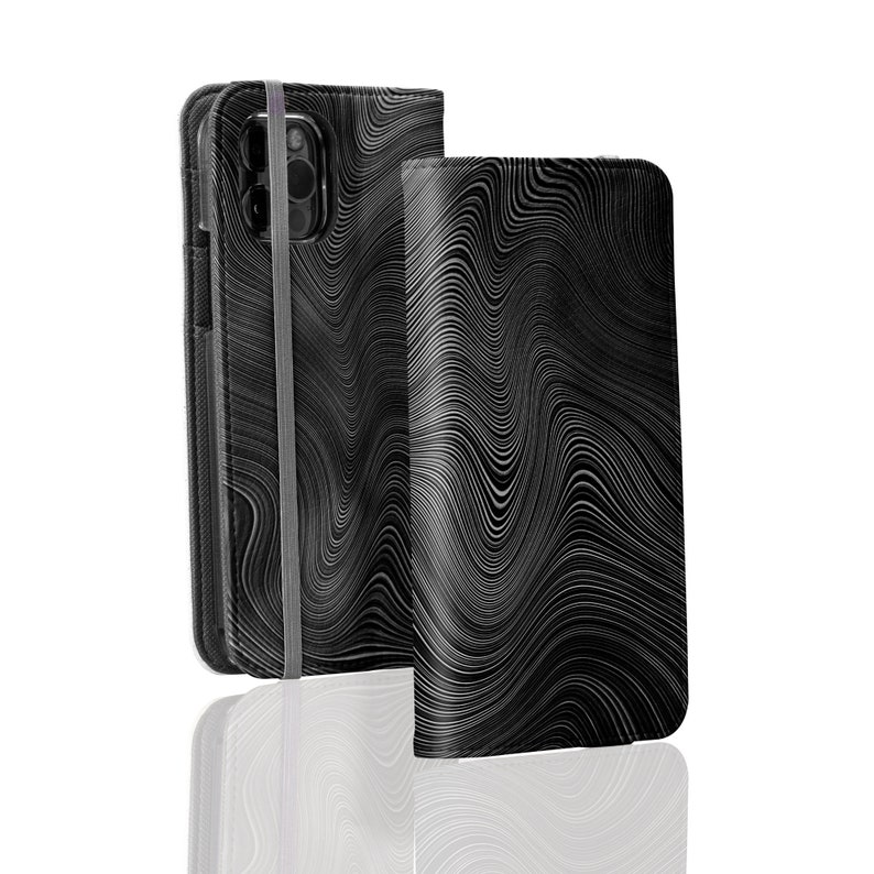 Może przedstawiać: Czarne etui na telefon z falistym, abstrakcyjnym wzorem. Etui ma klapkę, kt&oacute;ra składa się na ekran telefonu i pasek do zamykania.