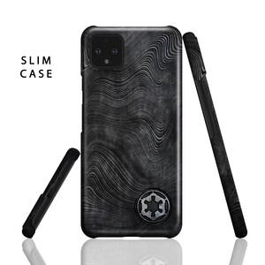 Puede incluir: Una funda de tel&eacute;fono negra con un patr&oacute;n ondulado y un s&iacute;mbolo imperial plateado. La funda est&aacute; dise&ntilde;ada para un tel&eacute;fono con una lente de c&aacute;mara doble.