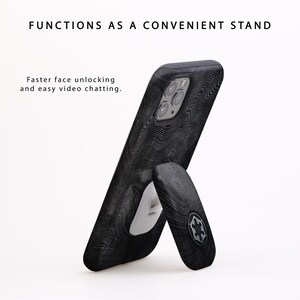K&ouml;nnte beinhalten: Eine schwarze Handyh&uuml;lle mit Holzmaserung und einem integrierten St&auml;nder. Die Handyh&uuml;lle ist so konzipiert, dass sie als praktischer St&auml;nder f&uuml;r schnellere Gesichtsentsperrung und einfache Videochats dient.