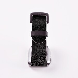May include: Black and white patterned watch band with a black leather strap. The band is designed for a smartwatch.