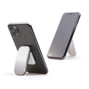 Puede incluir: Dos teléfonos inteligentes negros con un soporte blanco. El soporte es una pequeña pieza de plástico rectangular plana que se pliega para crear un soporte para el teléfono. Los teléfonos están en posición vertical, con las pantallas mirando hacia adelante.