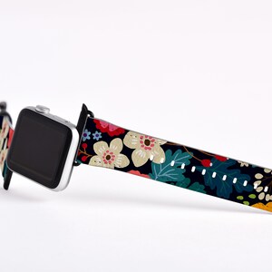Op de afbeelding: Een zwart Apple Watch bandje met een bloemenprint met witte, roze, rode, gele en groene bloemen op een donkere achtergrond.