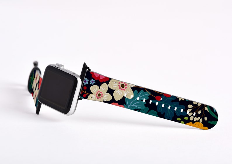 Op de afbeelding: Een zwart Apple Watch bandje met een bloemenprint met witte, roze, rode, gele en groene bloemen op een donkere achtergrond.