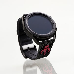 Op de afbeelding: Een zwarte smartwatch met een zwarte band met een rood en zwart Mandalorian-symbool. Het horloge heeft een zwarte wijzerplaat en de band heeft een textuur.
