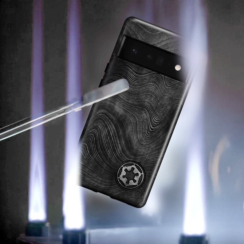 Puede incluir: Una funda para tel&eacute;fono negro con un patr&oacute;n texturizado ondulado y un s&iacute;mbolo en blanco y negro. La funda est&aacute; siendo sostenida por un par de manos, y hay llamas a cada lado de la funda.