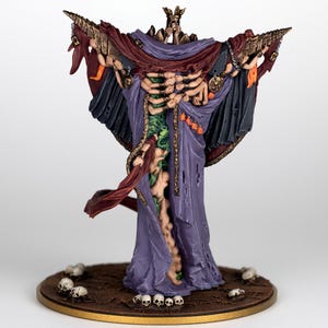 May include: A detailed figurine of a skeletal figure in a purple robe with outstretched arms. The figure has a crown and is adorned with small skulls and chains. The base is brown with scattered miniature skulls.