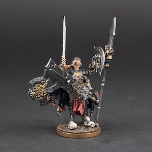 May include: A miniature fantasy figure of a skeletal warrior, holding a large black sword and a spear. The figure is clad in black armor with gold accents, and stands on a circular base with skulls. The figure is approximately 7.6 cm tall.