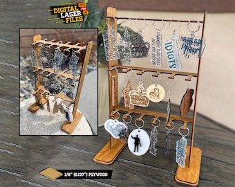 May include: A wooden display stand with three tiers for holding keychains. The stand is made of 1/8 inch plywood and has a natural wood finish. The keychains are made of various materials, including acrylic, metal, and wood. The keychains feature different designs, including text, images, and logos. The text on the keychains includes "IDIOTS", "I'm surrounded by", "where the HELL", "ape my vers?", "This girl is a Pfizer", and "CNP WIPNE".