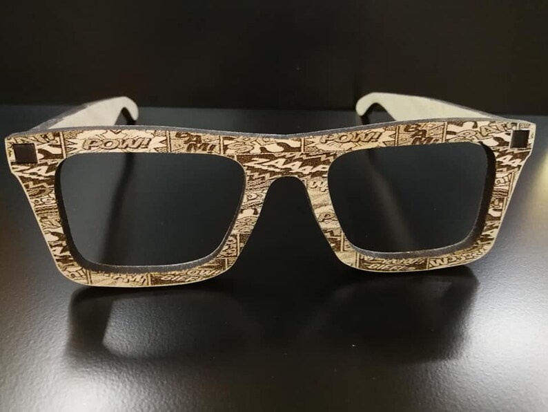 Puede incluir: Un par de gafas de sol de madera marr&oacute;n con lentes negras. Las monturas est&aacute;n decoradas con una impresi&oacute;n de c&oacute;mic con las palabras "POW!" y "BAM!"