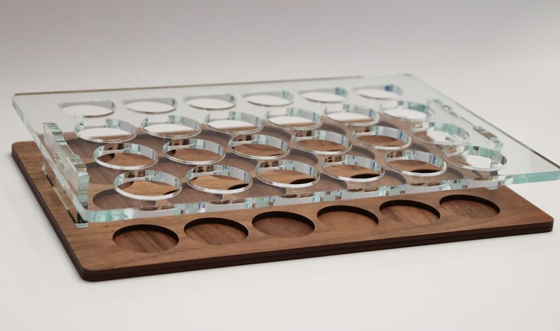 May include: A clear acrylic tray with 24 circular cutouts sits on top of a wooden tray with 12 circular cutouts. Both trays are made of wood.