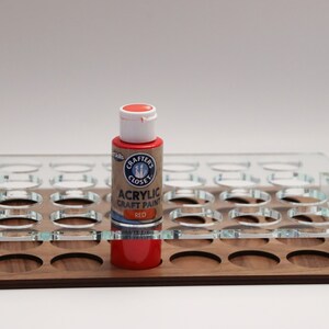 May include: A red acrylic craft paint bottle in a clear acrylic paint organizer with a wooden base. The bottle has a white lid and the label reads "Crafter's Closet Acrylic Craft Paint Red".