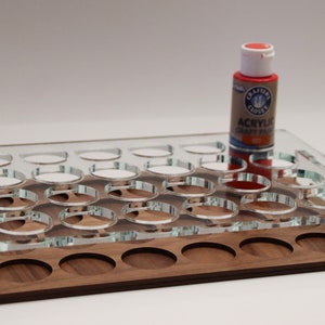 May include: A clear acrylic paint organizer with 24 round slots, a wooden base with 12 round slots, and a red acrylic paint bottle on top.