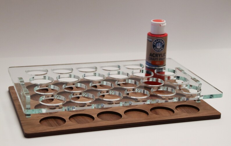 May include: A clear acrylic paint organizer with 24 round slots, a wooden base with 12 round slots, and a red acrylic paint bottle on top.