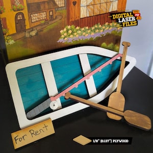 Op de afbeelding: Een houten bootmodel met een wit frame, een turquoise interieur en een roze hengel. Het model bevat twee houten roeispanen en een bord met de tekst "For Rent". De achtergrond toont een geschilderde scène van een dorp.