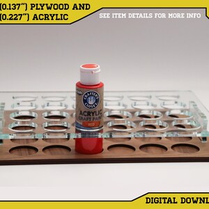 May include: A paint rack made of 1/8 inch plywood and 1/4 inch acrylic with 24 round slots for paint bottles. A red acrylic craft paint bottle is sitting in one of the slots.