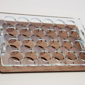 May include: A clear acrylic tray with 24 circular cutouts sits on top of a wooden base. The tray is designed to hold small round objects, such as bottle caps or coins.
