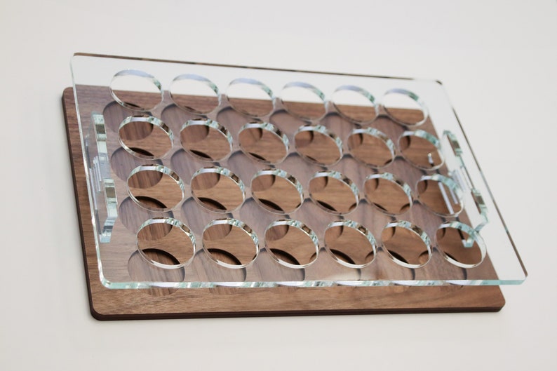 May include: A clear acrylic tray with 24 circular cutouts sits on top of a wooden base. The tray is designed to hold small round objects, such as bottle caps or coins.