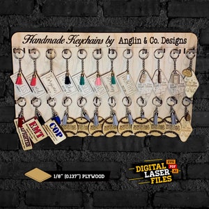 Puede incluir: Un tablero de exhibición de madera con 18 llaveros de madera diferentes cortados con láser. Los llaveros presentan varios diseños, incluyendo pelotas de béisbol, borlas y palabras como "Papá", "EMT" y "Policía". El tablero está etiquetado como "Llaveros hechos a mano por Anglin & Co. Designs".