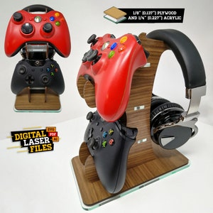 Puede incluir: Un soporte de madera con dos mandos de videojuegos negros y rojos y unos auriculares negros. El soporte está hecho de madera contrachapada de 1/8 de pulgada y acrílico de 1/4 de pulgada. El soporte está etiquetado como "Archivos de láser digital" con los tipos de archivos SVG, PDF y AI.