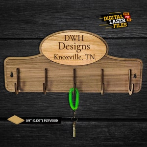 Peut inclure: Porte-clés en bois avec quatre crochets et une plaque indiquant "DWH Designs Knoxville, TN.". La plaque est de forme ovale et a une finition en bois brun. Le porte-clés est fait de contreplaqué de 1/8 de pouce.