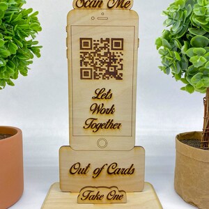 Op de afbeelding: Houten standaard in de vorm van een smartphone met een QR-code, de tekst "Scan Me", "Let's Work Together", "Out of Cards" en "Take One".