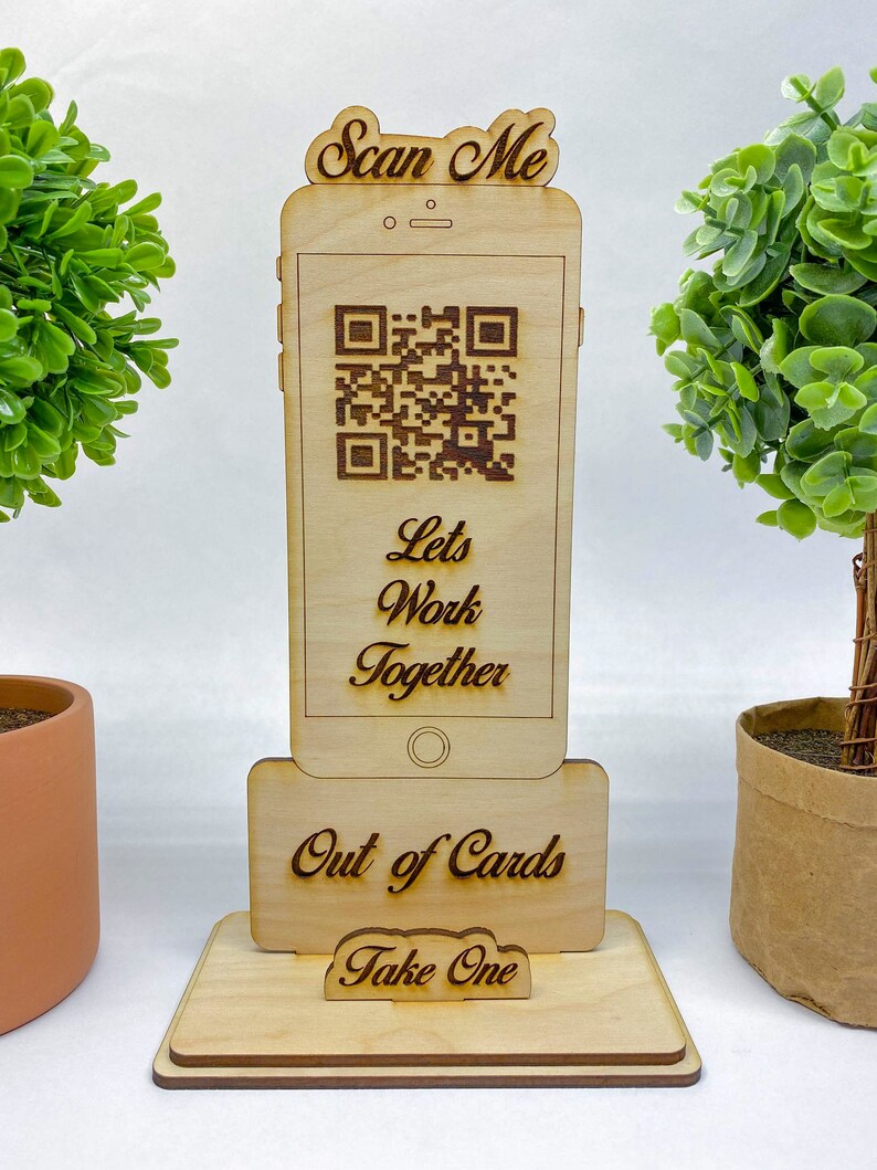 Op de afbeelding: Houten standaard in de vorm van een smartphone met een QR-code, de tekst "Scan Me", "Let's Work Together", "Out of Cards" en "Take One".