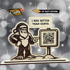 May include: Wooden Christmas decoration featuring a Bigfoot wearing a Santa hat. The Bigfoot points to a sign with a QR code and the text "I HIDE BETTER THAN SANTA". The sign is made of 1/8" plywood.