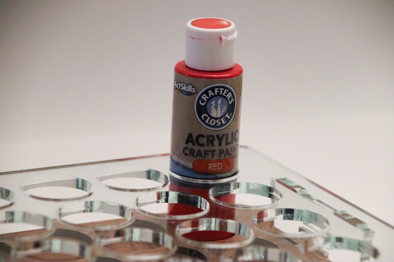 May include: A small bottle of red acrylic craft paint with a white lid and label. The label says "Crafter's Closet" and "Acrylic Craft Paint" in black text. The word "Red" is printed in white text on a blue background.