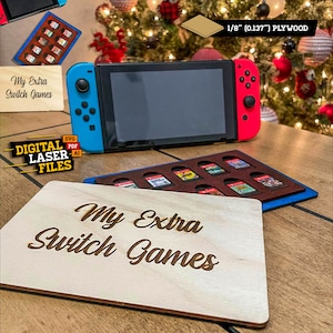 Może przedstawiać: Drewniany uchwyt na kartridże do gier z napisem "My Extra Switch Games" wyciętym laserowo na jasnym drewnie. Uchwyt jest przeznaczony do przechowywania kartridży do gier Nintendo Switch. Widoczna jest również konsola Nintendo Switch.