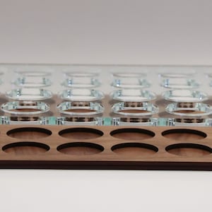 May include: A wooden tray with a clear glass top. The tray has 24 circular cutouts for holding small items. The tray is made of walnut wood and has a natural finish.